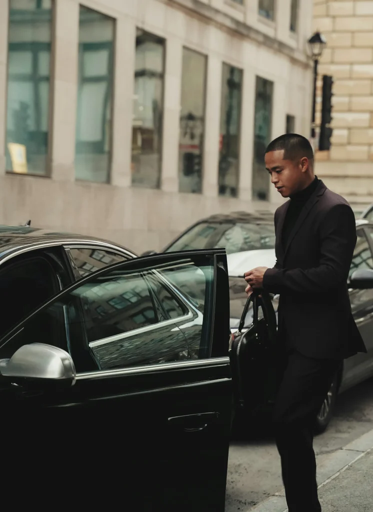 Chauffeur in a black tuxedo standing beside a luxury car